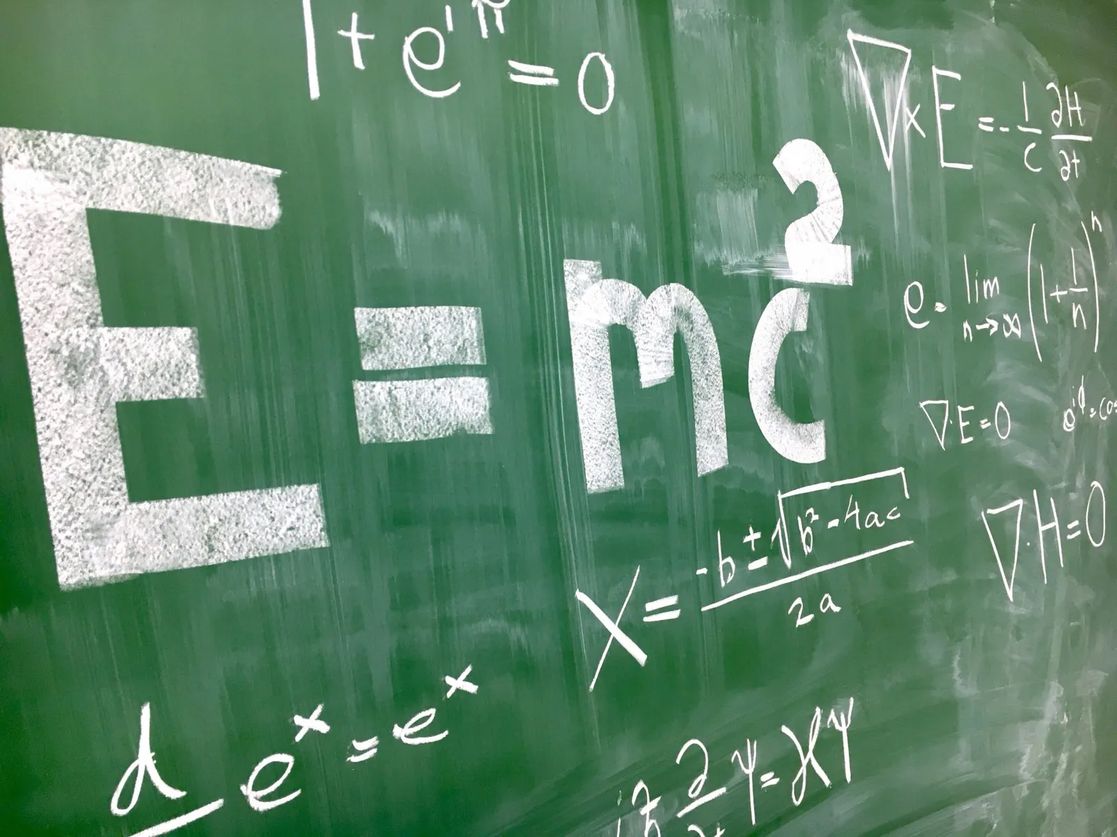 Tableau vert couvert de formules de physique écrites à la craie, dont E = mc².
